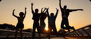 Silhouettes of people celebrating with raised arms against sunset